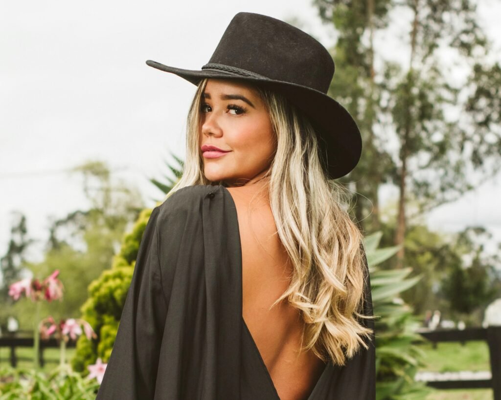 Chic woman with blonde hair wearing a black fedora outdoors, showcasing a backless outfit and confident pose.